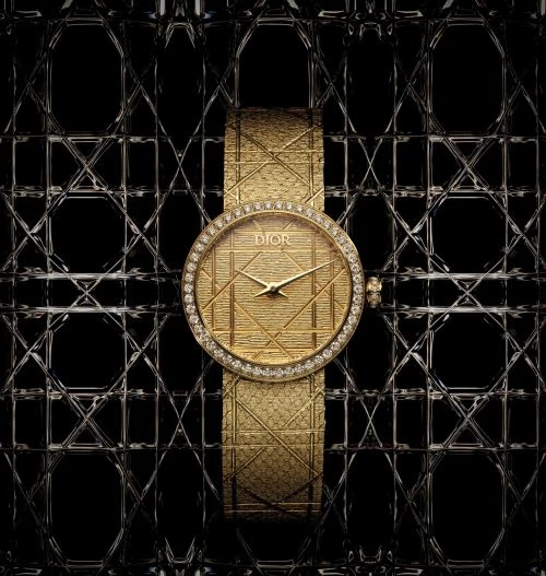 Elegant gold Dior watch with diamond bezel and textured strap set against a geometric, lattice-like black and silver background.