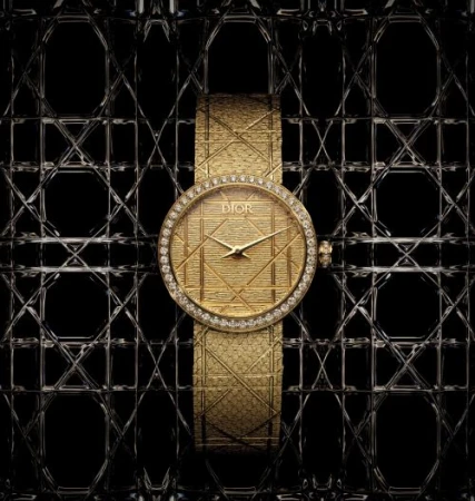 Elegant gold Dior watch with diamond bezel and textured strap set against a geometric, lattice-like black and silver background.