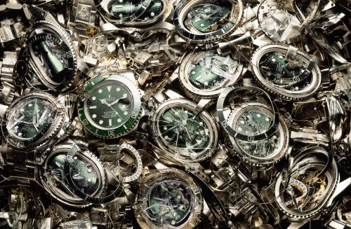 Pile of damaged and broken Rolex watches with shattered crystals and scratched metal, creating a chaotic and cluttered view.