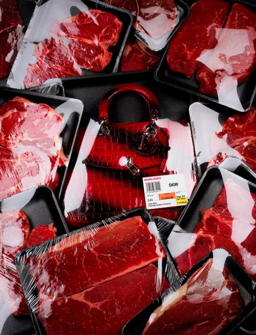 Overhead studio shot of a red leather handbag placed among several packages of raw meat wrapped in plastic and arranged on a black surface.