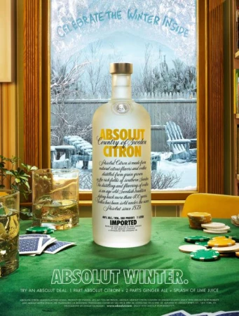 Absolut Citron vodka bottle stands on a poker table with a snowy winter scene visible through a window behind it.