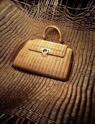 Woven straw handbag resting inside a matching woven wicker hammock structure with warm lighting.