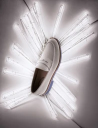 White leather loafer positioned centrally over glowing glass tubes radiating outward in a studio setting