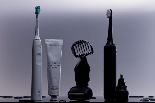 A collection of personal care items including electric toothbrushes, toothpaste, and a trimmer against a neutral background.