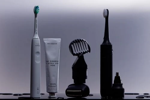 A collection of personal care items including electric toothbrushes, toothpaste, and a trimmer against a neutral background.