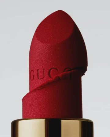 Extreme close-up macro shot of a red matte lipstick bullet featuring embossed lettering against a neutral grey background.