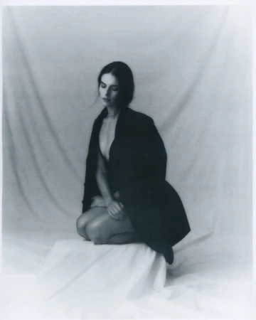 Monochrome portrait of a woman kneeling on a draped platform in a dark blazer, styled by Nicole Louie.