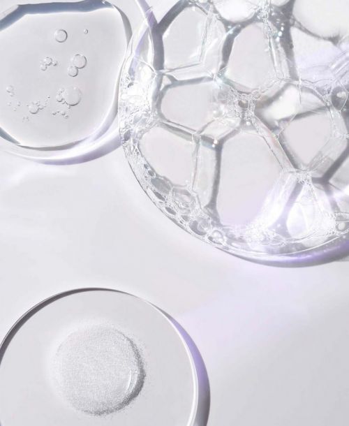 Close-up of transparent liquid with bubbles, gel, and powder, showcasing cosmetic product textures on a white surface with soft light.