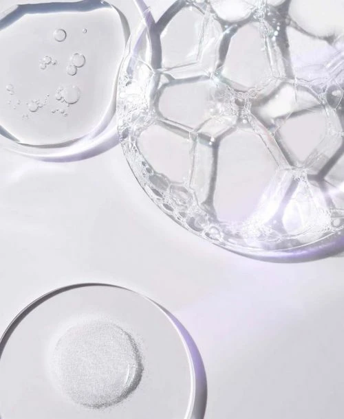 Close-up of transparent liquid with bubbles, gel, and powder, showcasing cosmetic product textures on a white surface with soft light.