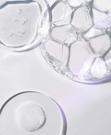 Close up overhead shot of clear gel textures, soapy bubbles, and white powder on a clean white surface