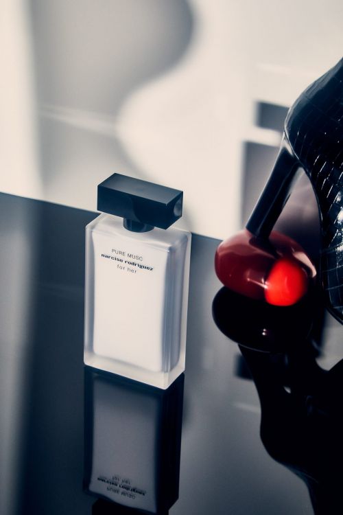 Elegant studio product shot of Narciso Rodriguez Pure Musc perfume bottle next to a high heel pump on a glossy surface with reflections.