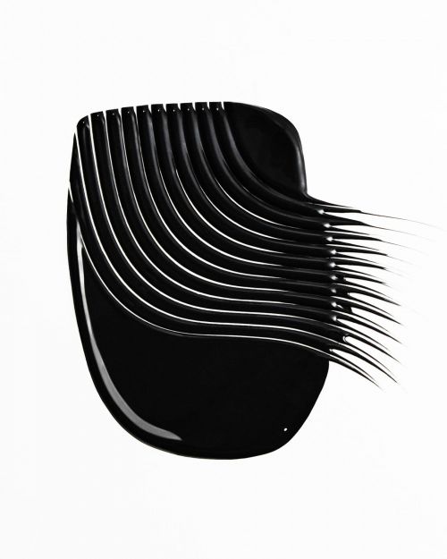 Close-up of a smear of black mascara. The makeup product is swiped in an arching pattern across a plain white surface. 