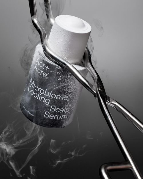Act+Acre microbiome cooling scalp serum held with metal tongs. Condensation and light water vapor give the product a frozen aesthetic.
