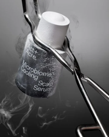 Act+Acre microbiome cooling scalp serum held with metal tongs. Condensation and light water vapor give the product a frozen aesthetic.