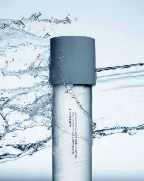 Product shot of LANEIGE Water Bank toner bottle with water splashing around it. The bottle is light blue and translucent.