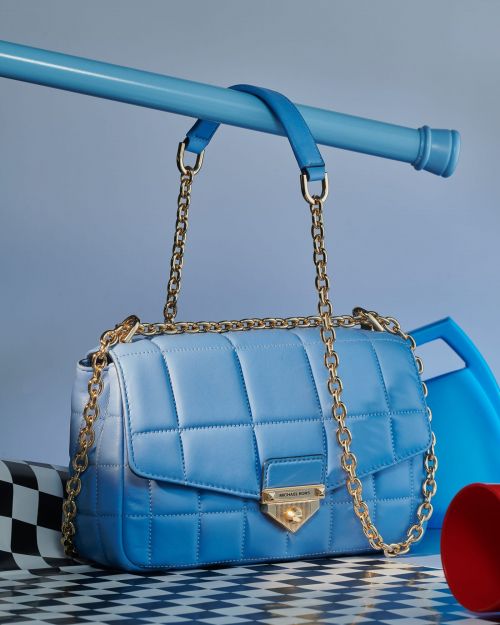 Blue quilted leather satchel with gold chain strap and hardware sitting on a black and white checkered surface in a studio setting.