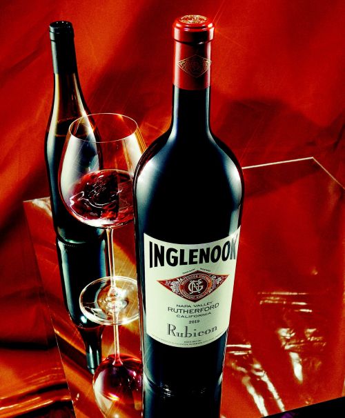 Close-up product shot of a dark glass wine bottle with a white label and red foil cap resting on a reflective surface