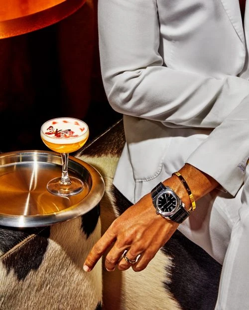 Cocktail on a silver tray with an adult wearing a white suit and a watch, seated on a brown and white animal print bench seat.