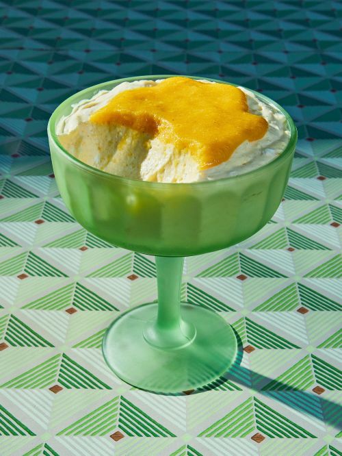 Green stemmed dessert bowl with white and yellow cream dessert on a geometric pattern table, studio lighting, food photography.