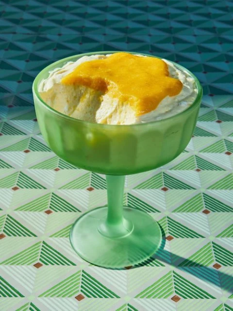 Green stemmed dessert bowl with white and yellow cream dessert on a geometric pattern table, studio lighting, food photography.