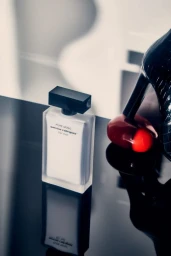 Narciso Rodriguez perfume bottle resting on a glossy black reflective surface next to a high heel shoe