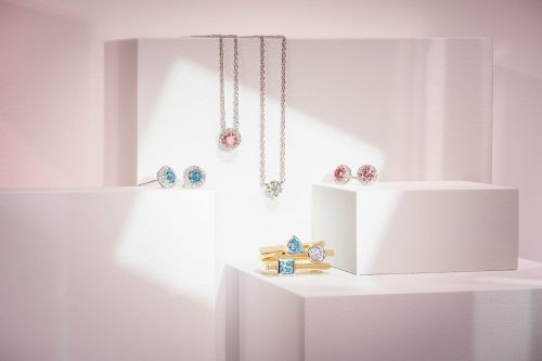 Elegant jewelry still life on white display cubes with necklaces and earrings featuring gemstones in pastel pinks and blues.