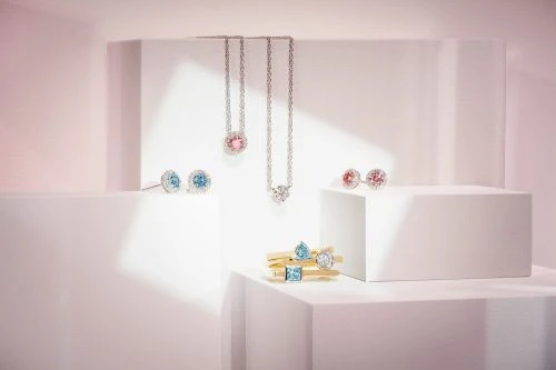 Elegant jewelry still life on white display cubes with necklaces and earrings featuring gemstones in pastel pinks and blues.