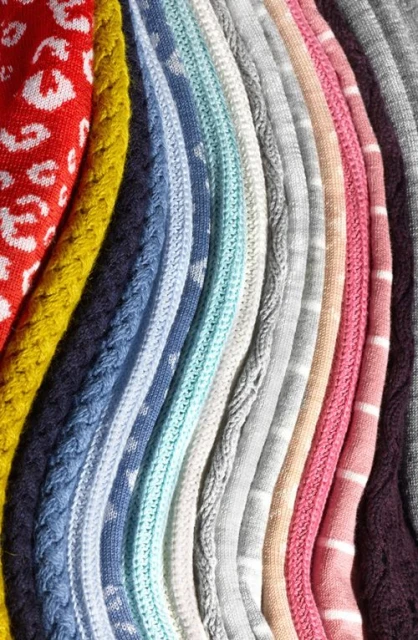 Close-up of colorful knitted fabrics with various patterns and textures, including cable knits, animal prints, and stripes.