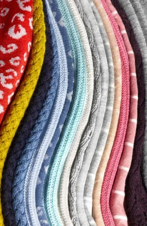 Close-up of colorful knitted fabrics with various patterns and textures, including cable knits, animal prints, and stripes.