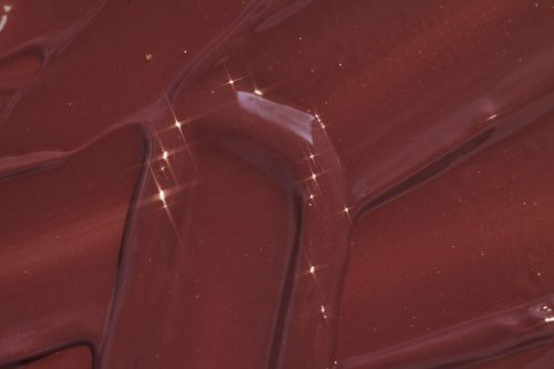 Close-up shot of glossy, textured brown material with light reflections, creating abstract patterns. The surface shows depth and shine.