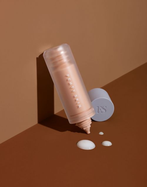 Fenty Skin product bottle with serum drops on a brown surface in a studio environment for beauty and skincare promotions.
