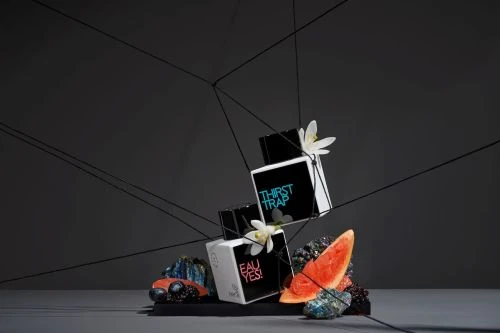 Artful display of stacked perfume boxes with floral accents and geometric string design against a dark backdrop in studio setting.