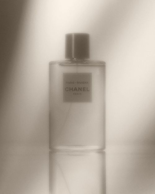 Close-up studio shot of a clear glass Chanel perfume bottle, showcasing its label and subtle reflections against a diffused background.