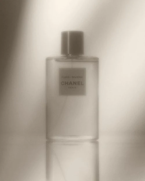 Close-up studio shot of a clear glass Chanel perfume bottle, showcasing its label and subtle reflections against a diffused background.