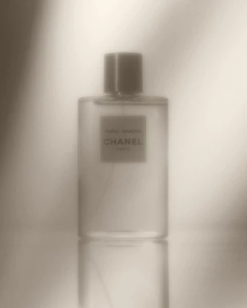Close-up studio shot of a clear glass Chanel perfume bottle, showcasing its label and subtle reflections against a diffused background.