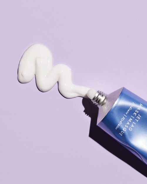 Close-up shot of a blue tube of Jet Lag Mask with a swirl of white cream on a purple surface, showcasing beauty and skincare.