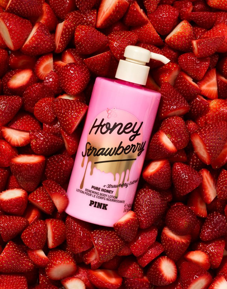Pink bottle of Honey Strawberry body lotion set against a background of fresh strawberries, creating a vibrant beauty product shot.