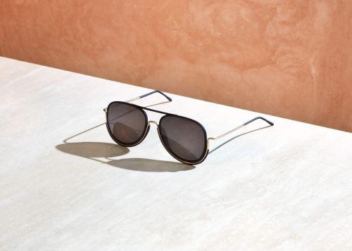 Studio shot of aviator sunglasses with black frames and grey lenses on a marble table, reflecting sunlight against a textured background.