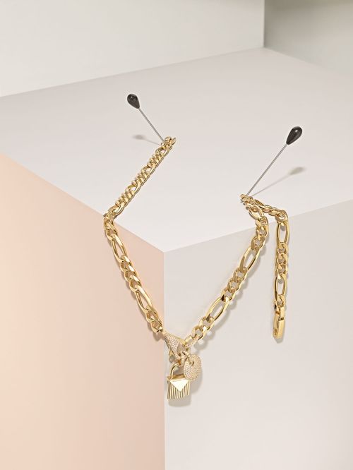 Gold chain necklace with charms displayed against a geometric white and pastel pink background, secured with stick pins.