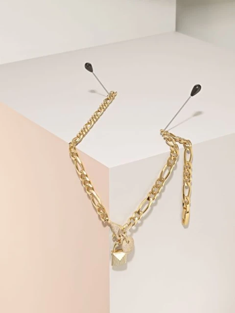 Gold chain necklace with charms displayed against a geometric white and pastel pink background, secured with stick pins.