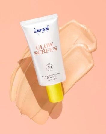 Supergoop! Glow Screen SPF 40 sunscreen tube on a beige swatch, presented on a pale pink background, in a beauty product shot.