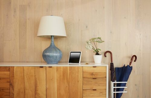 Interior view of a wooden cabinet topped with a blue lamp, a tablet, a plant, and umbrellas, set against a light wood paneled wall.