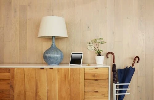 Interior view of a wooden cabinet topped with a blue lamp, a tablet, a plant, and umbrellas, set against a light wood paneled wall.