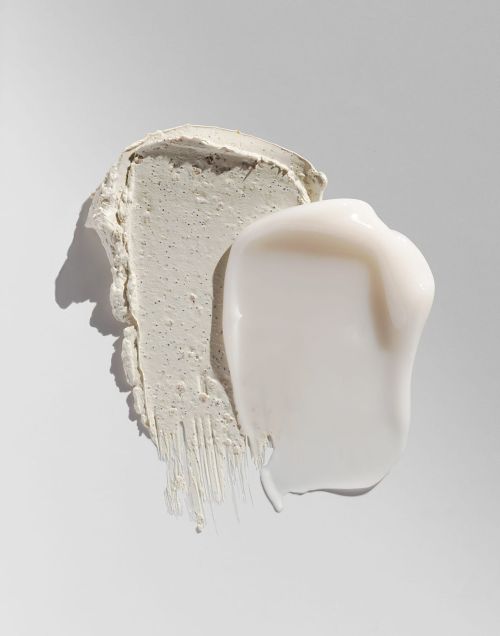 Close-up of two different facial cream smears or strokes on a white surface. One creamy white, one textured grey.