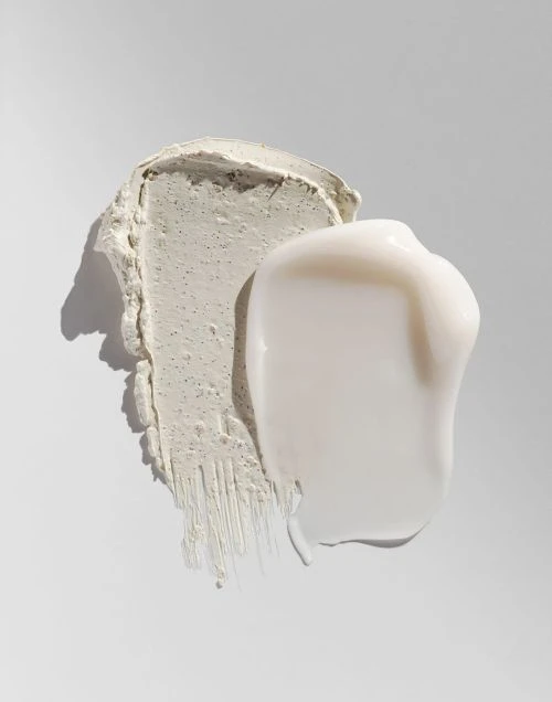 Close-up of two different facial cream smears or strokes on a white surface. One creamy white, one textured grey.