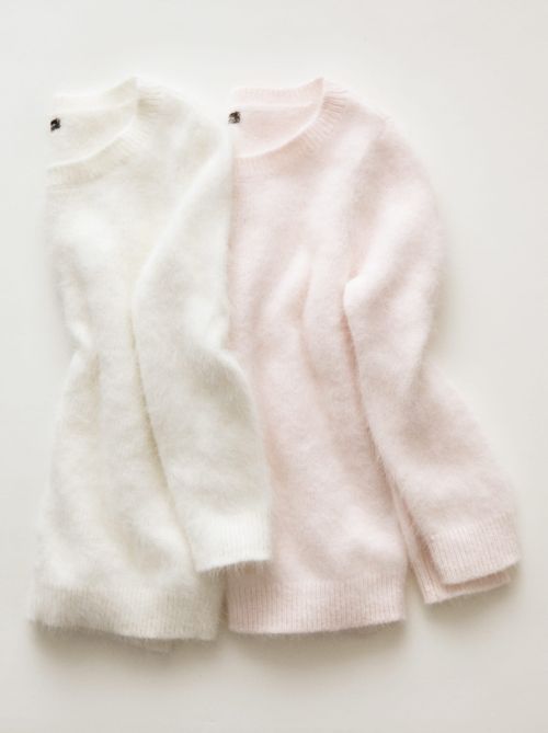 Two folded sweaters, one white and one light pink, are presented against a stark white backdrop in a fashion-focused still life composition.