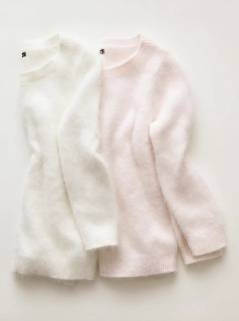 Two folded sweaters, one white and one light pink, are presented against a stark white backdrop in a fashion-focused still life composition.