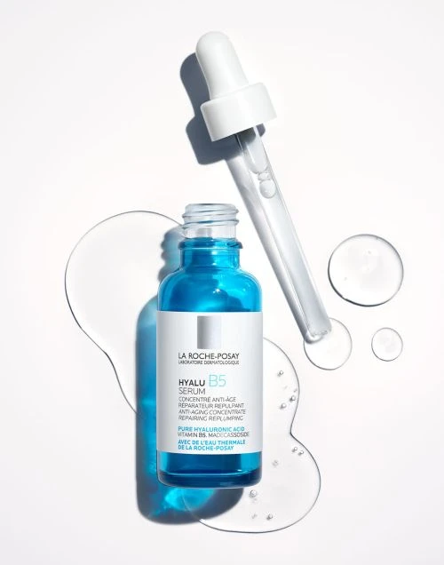 La Roche-Posay Hyalu B5 serum in blue bottle with dropper and water droplets on a white surface. Beauty and skincare product.