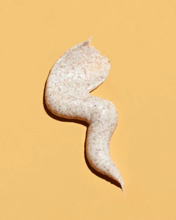 A swirl of exfoliating scrub with grainy texture is on a smooth, light peach background in a beauty or personal care setting.