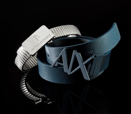 Two Armani Exchange (AX) logo belts, one metallic and the other blue leather, are displayed against a black background.